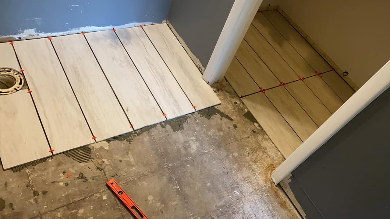 Bathroom floor tile installation in progress around the toilet flange